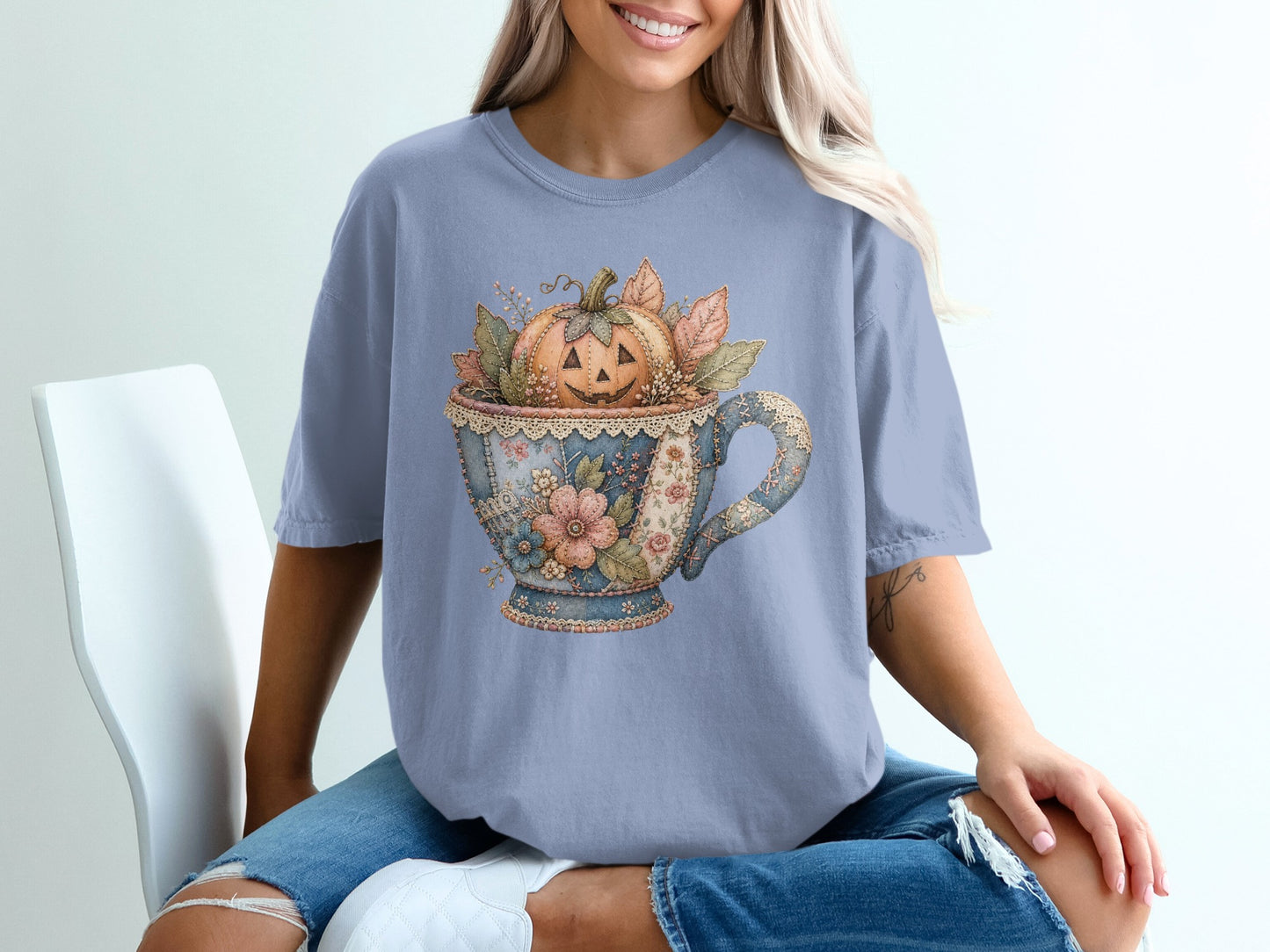 T-shirt with a blue teacup graphic filled with a carved pumpkin and autumn leaves.