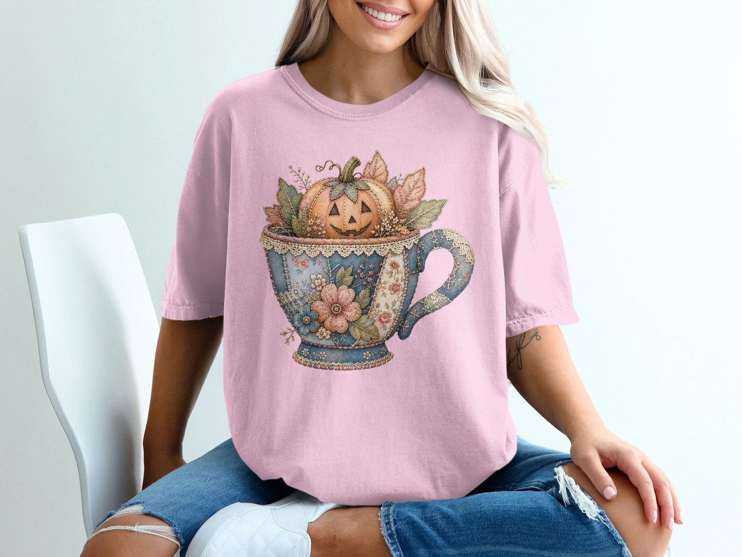 Pink t-shirt with stitched floral teacup holding a jack-o'-lantern and autumn leaves.
