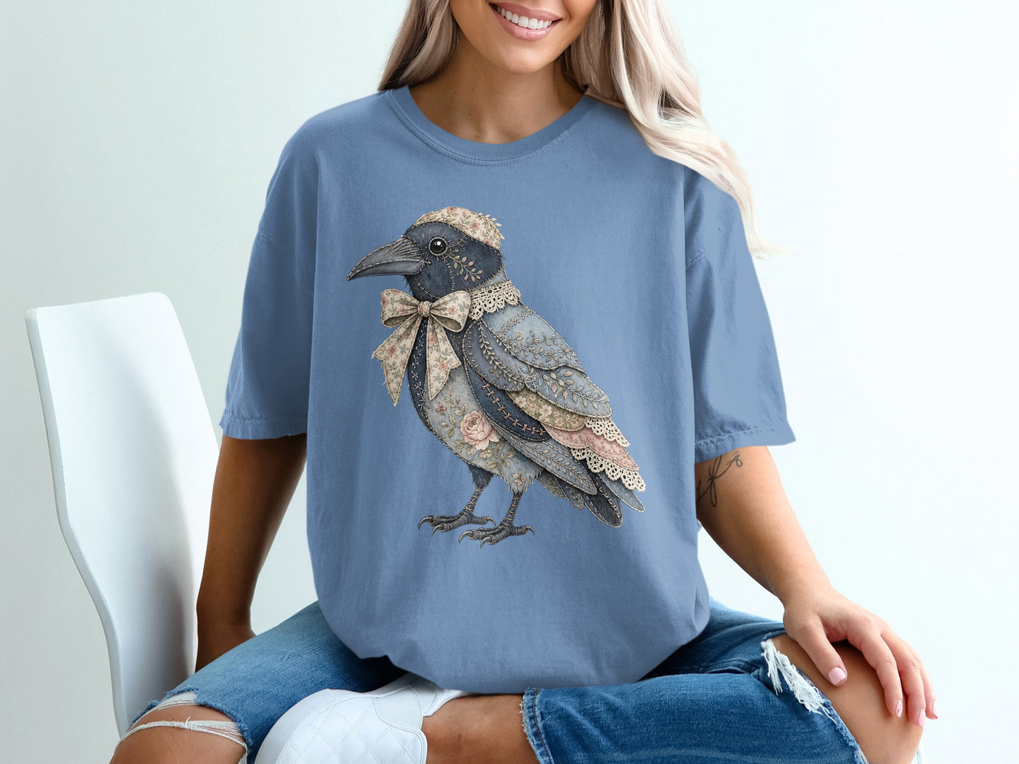 Blue t-shirt with a patched crow graphic wearing a floral bow and lace collar.