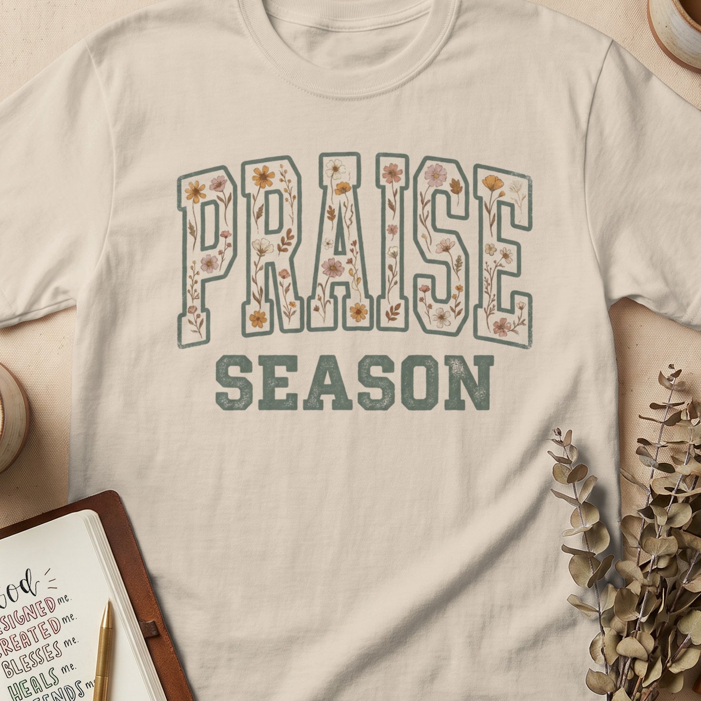 Light beige t-shirt with "PRAISE SEASON" text featuring floral fill and outline.