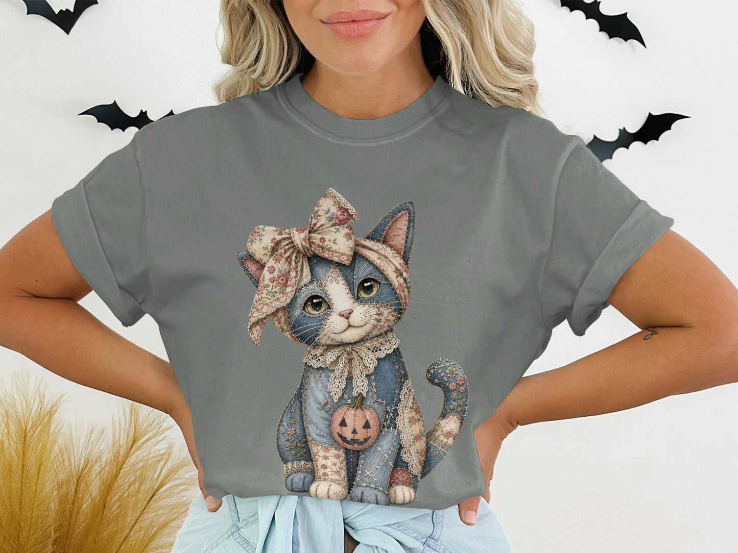 Gray t-shirt featuring a fabric-textured cat wearing a floral bow and holding a pumpkin.