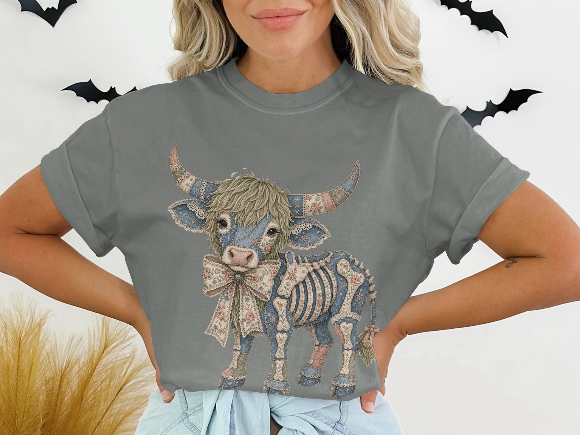Highland cow graphic shirt with floral and skeleton details and a bow.