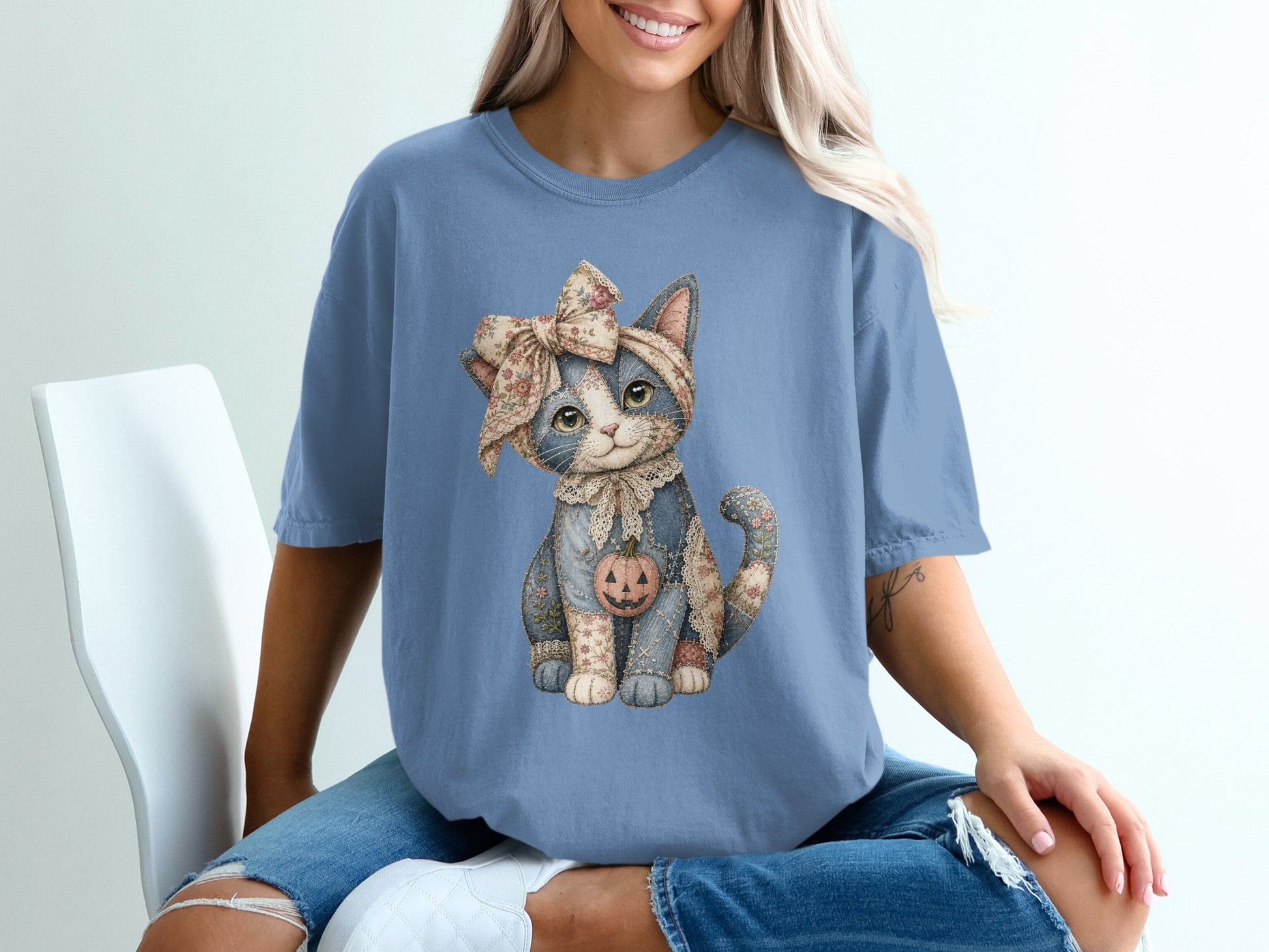 Blue t-shirt with a front graphic of a patchwork cat wearing a floral bow and a jack-o'-lantern.