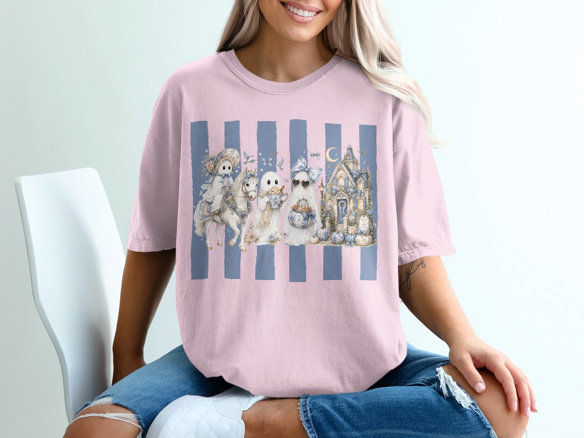 Pink t-shirt with a watercolor Halloween graphic of ghosts, a haunted house, and a unicorn.