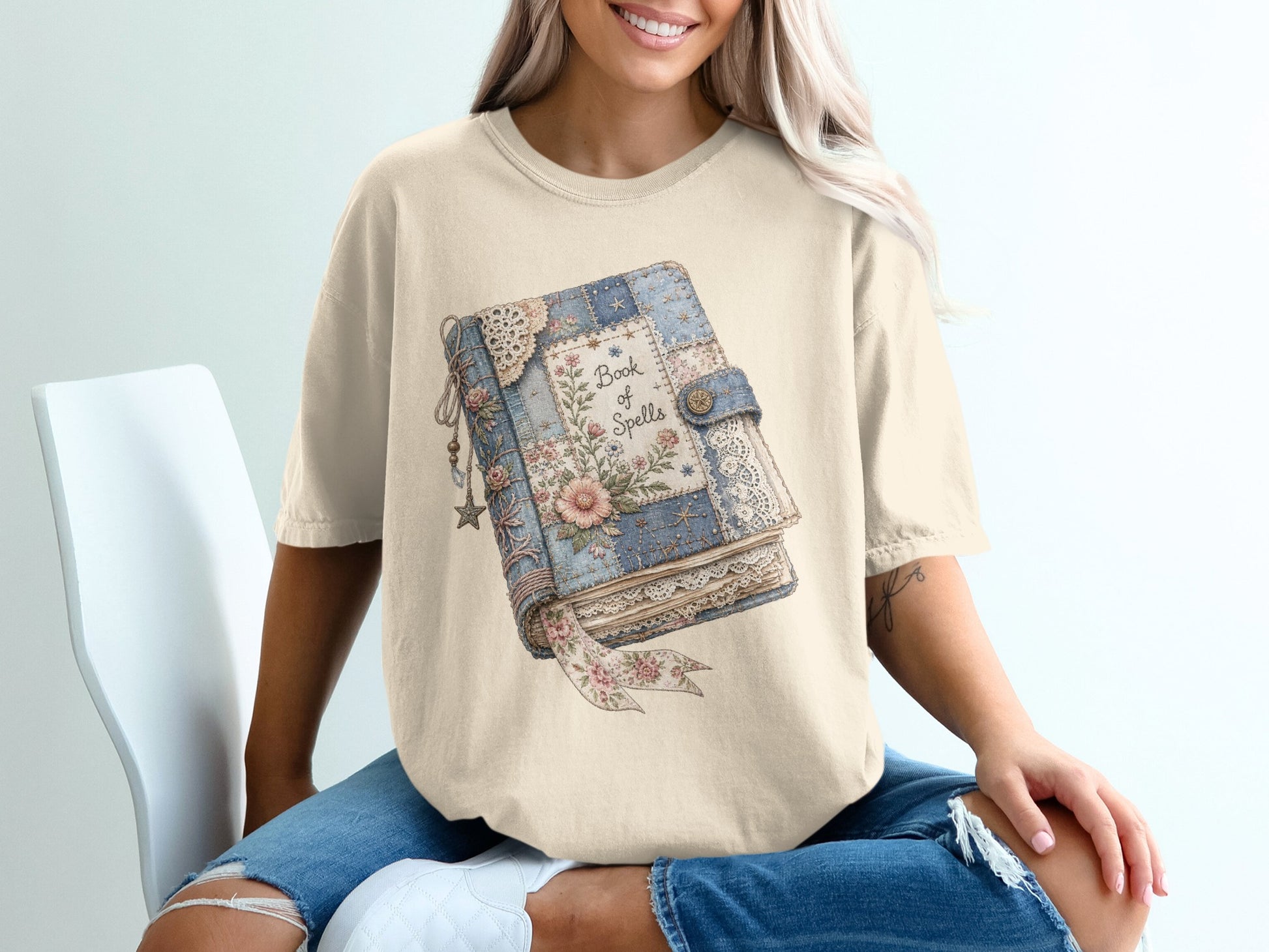 Cream t-shirt featuring a graphic of an old book titled "Book of Spells".