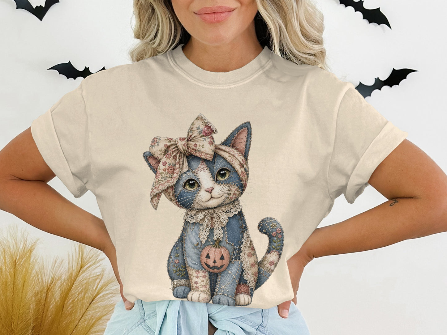 T-shirt graphic of a blue patchwork cat wearing a floral bow and holding a jack-o'-lantern.