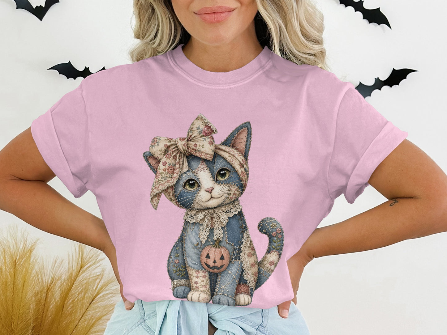 Pink t-shirt with a stitched cat graphic holding a jack-o'-lantern.