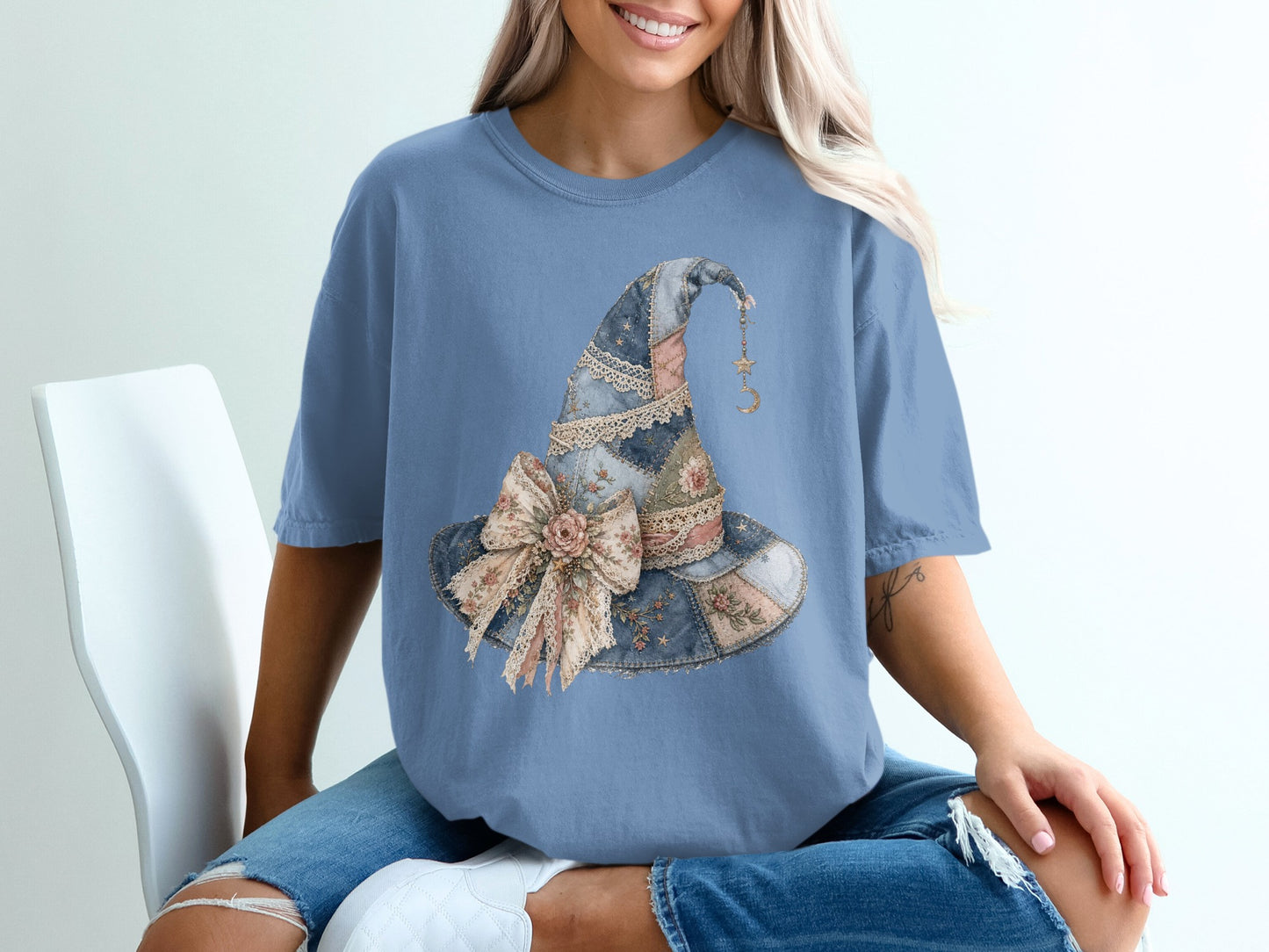 Blue t-shirt with a watercolor patchwork witch hat graphic featuring a ribbon bow and dangling moon charm.