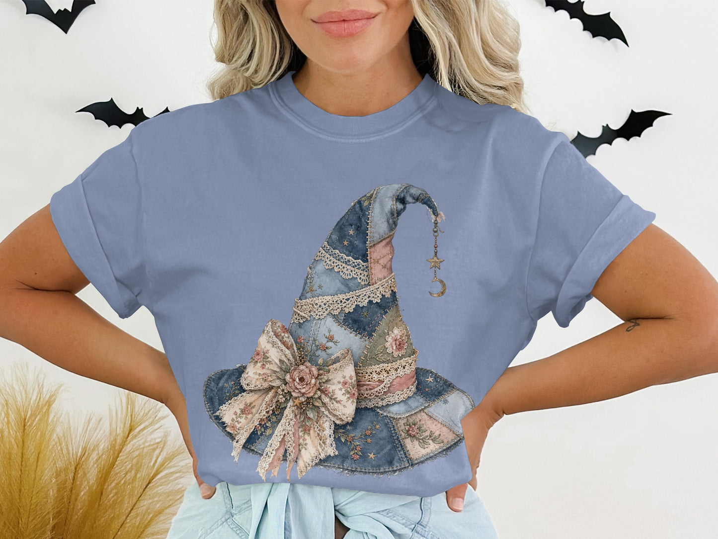 Blue t-shirt featuring a quilted patchwork witch hat graphic with floral details and a bow.