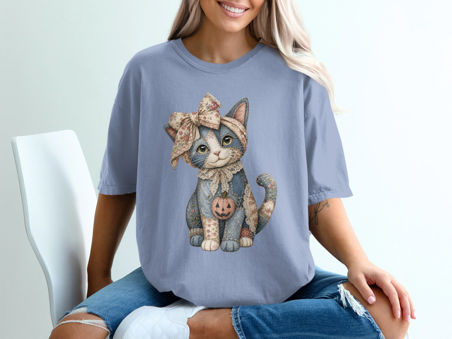 Blue t-shirt features a patched cat graphic wearing a floral bow and holding a pumpkin.