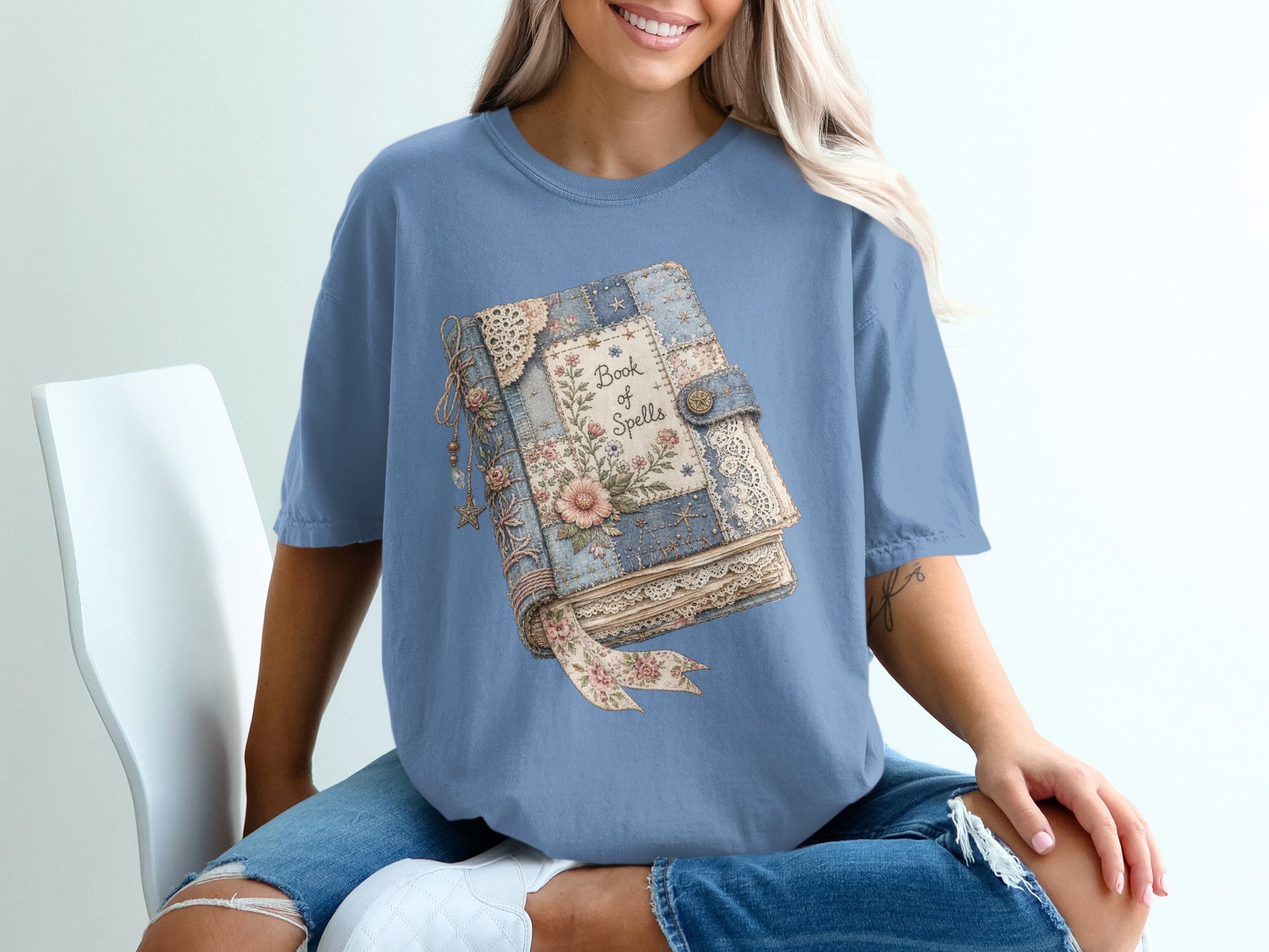 Blue t-shirt with a "Book of Spells" graphic of a vintage book with floral details.