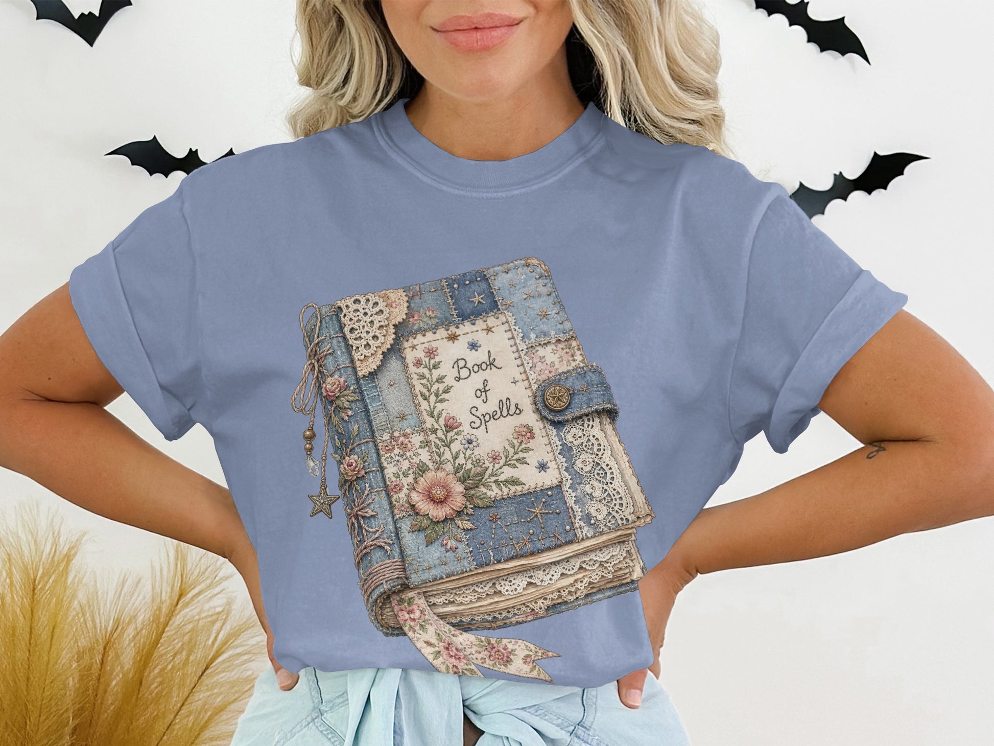Blue t-shirt with vintage book labeled "Book of Spells" and floral embellishments.