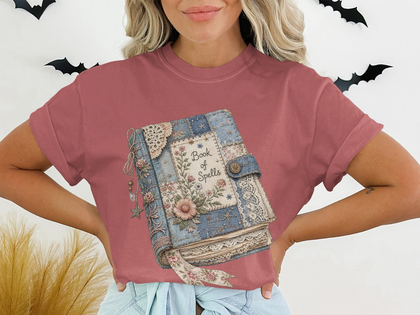 T-shirt graphic of a quilted book titled "Book of Spells" with floral and lace details.