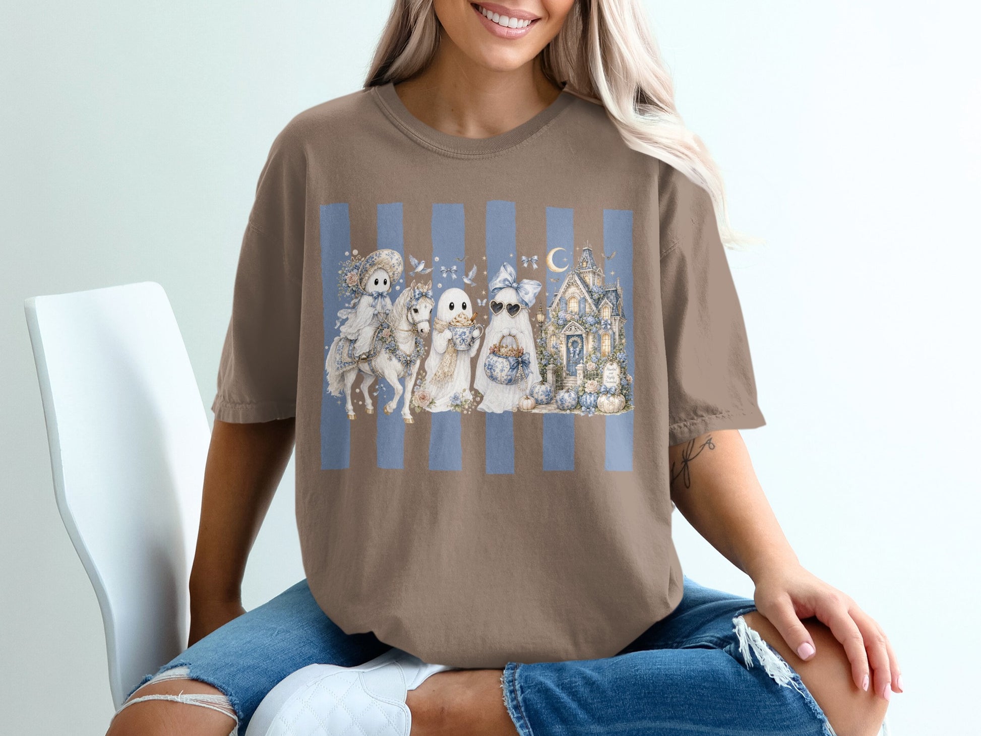 Brown t-shirt with a watercolor design of ghosts, a horse, and a haunted house on blue stripes.