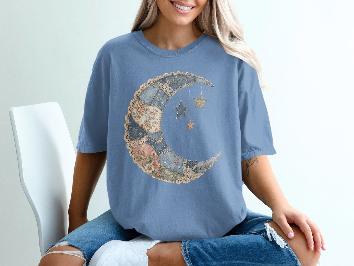 Blue t-shirt with a patchwork crescent moon and hanging stars graphic.