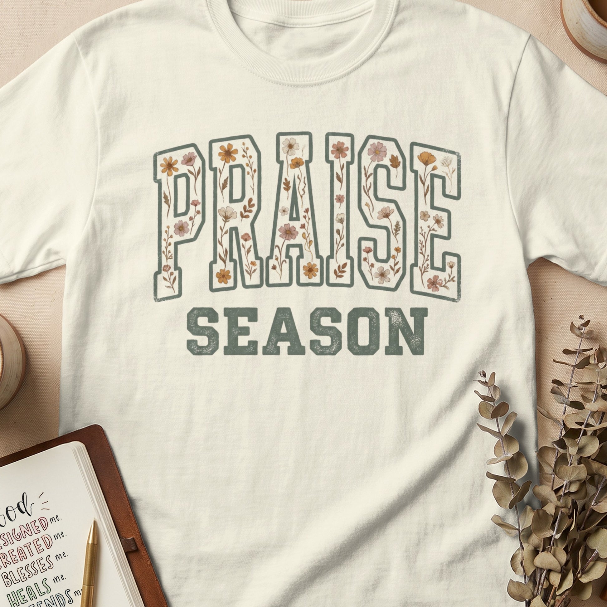 Cream t-shirt with "PRAISE SEASON" in floral collegiate font.