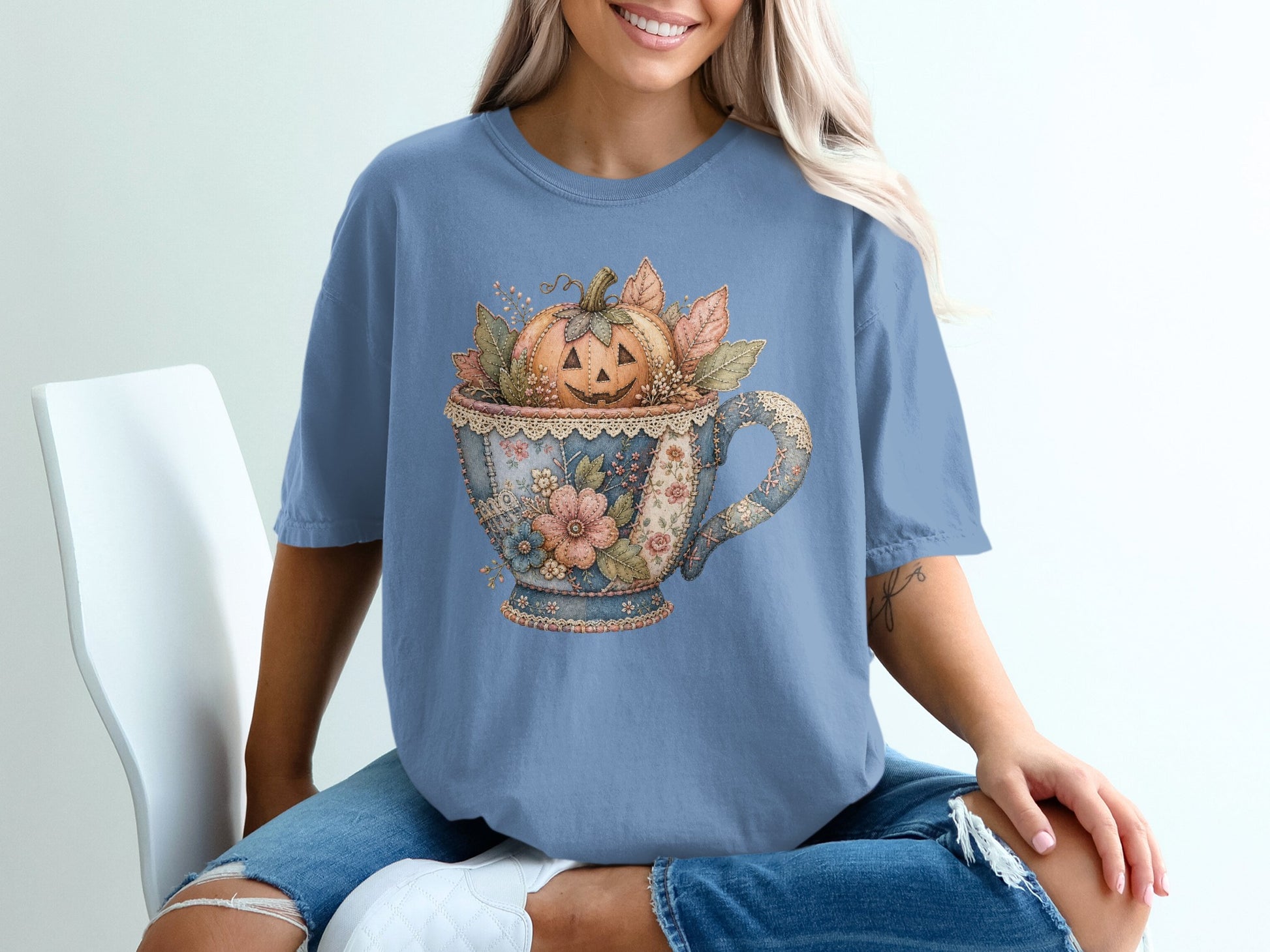 Blue t-shirt with a vintage teacup design featuring a carved jack-o'-lantern and autumn leaves.
