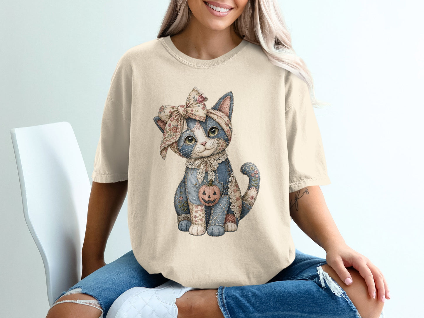 Cream t-shirt with a patchwork cat wearing a floral bow and holding a pumpkin.