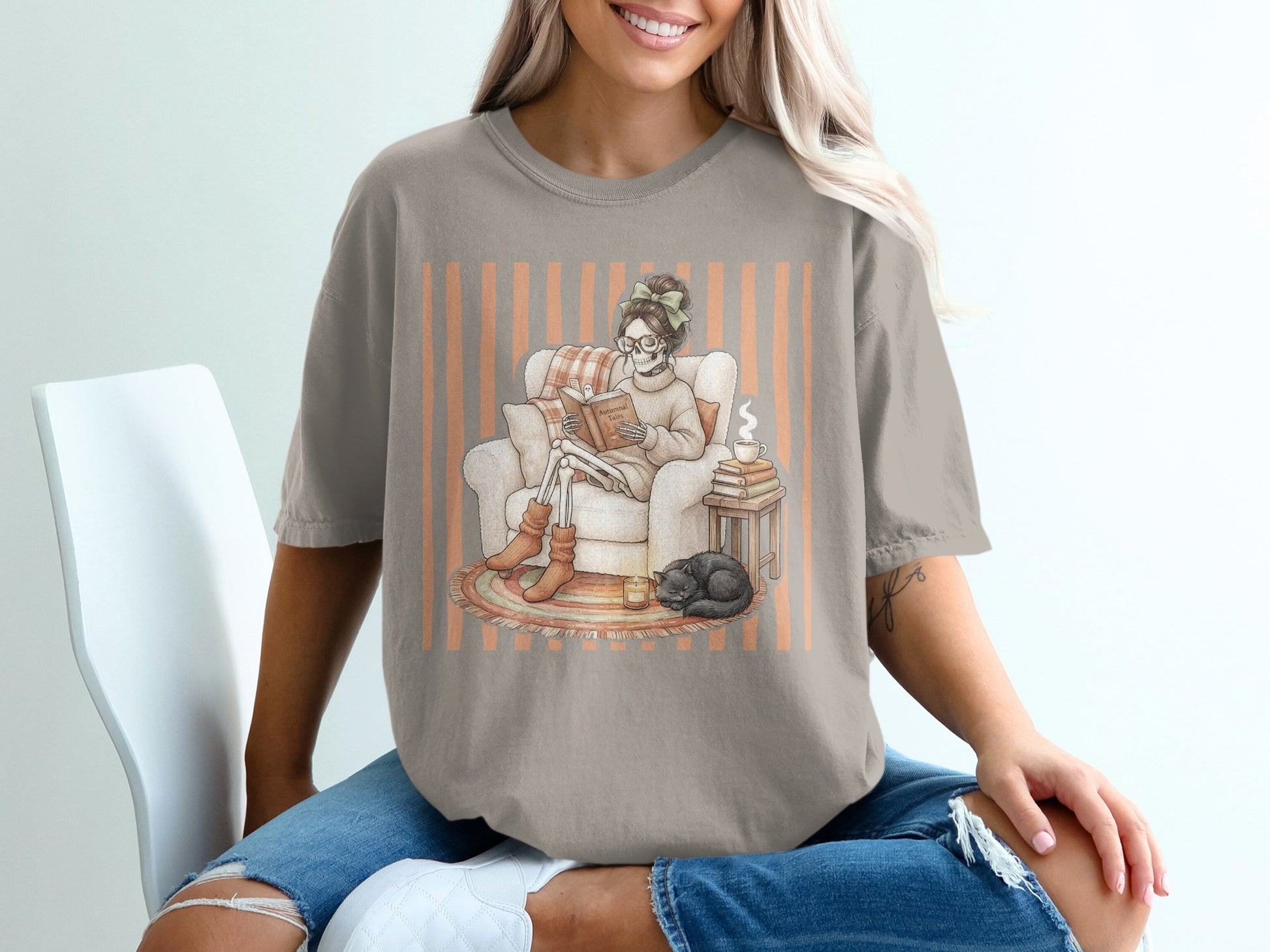 Skeleton woman reading "Autumnal Tales" curled up in chair with cat.