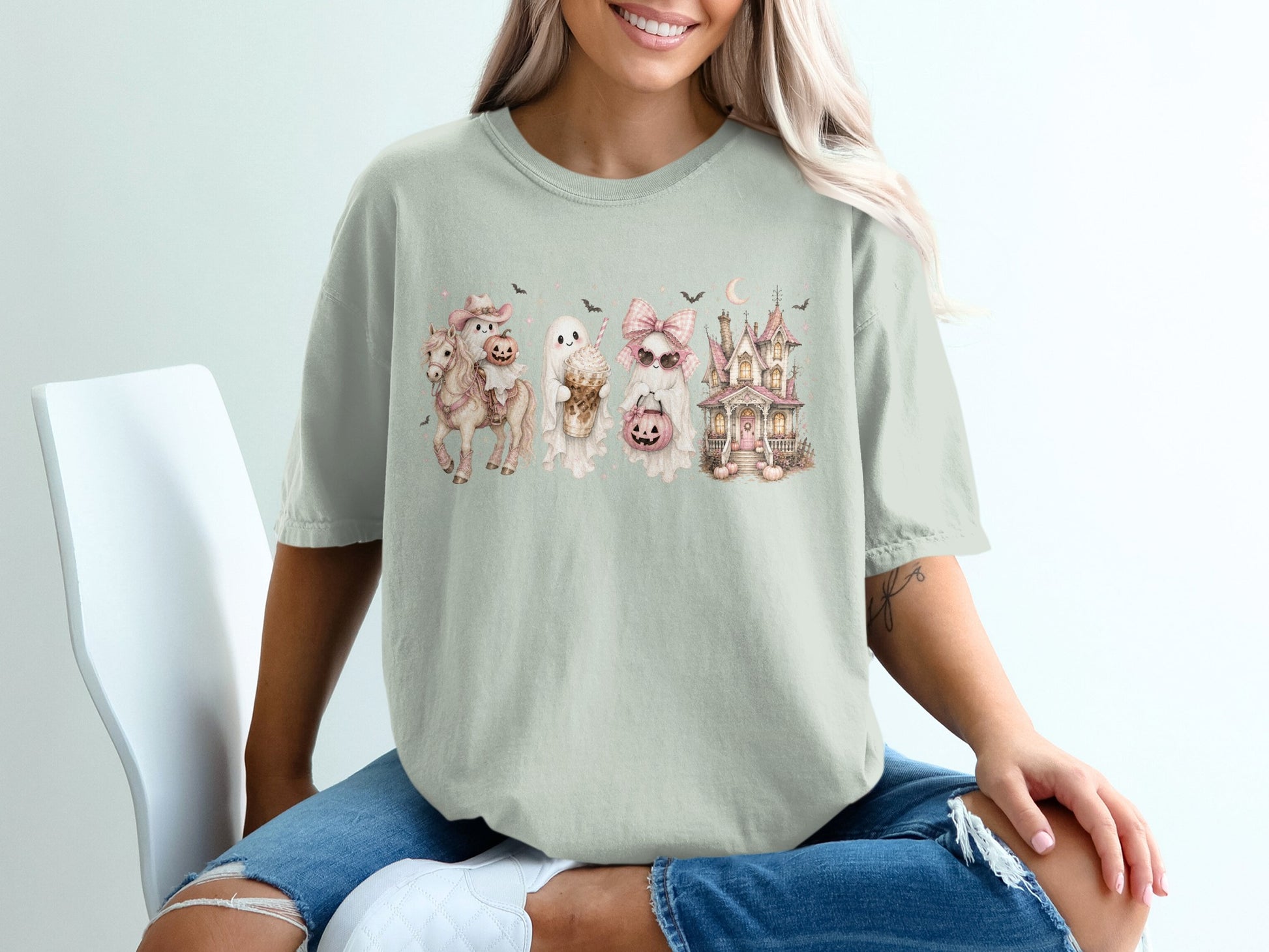Light green t-shirt with a pastel Halloween graphic of a horse, ghosts, and a haunted house.