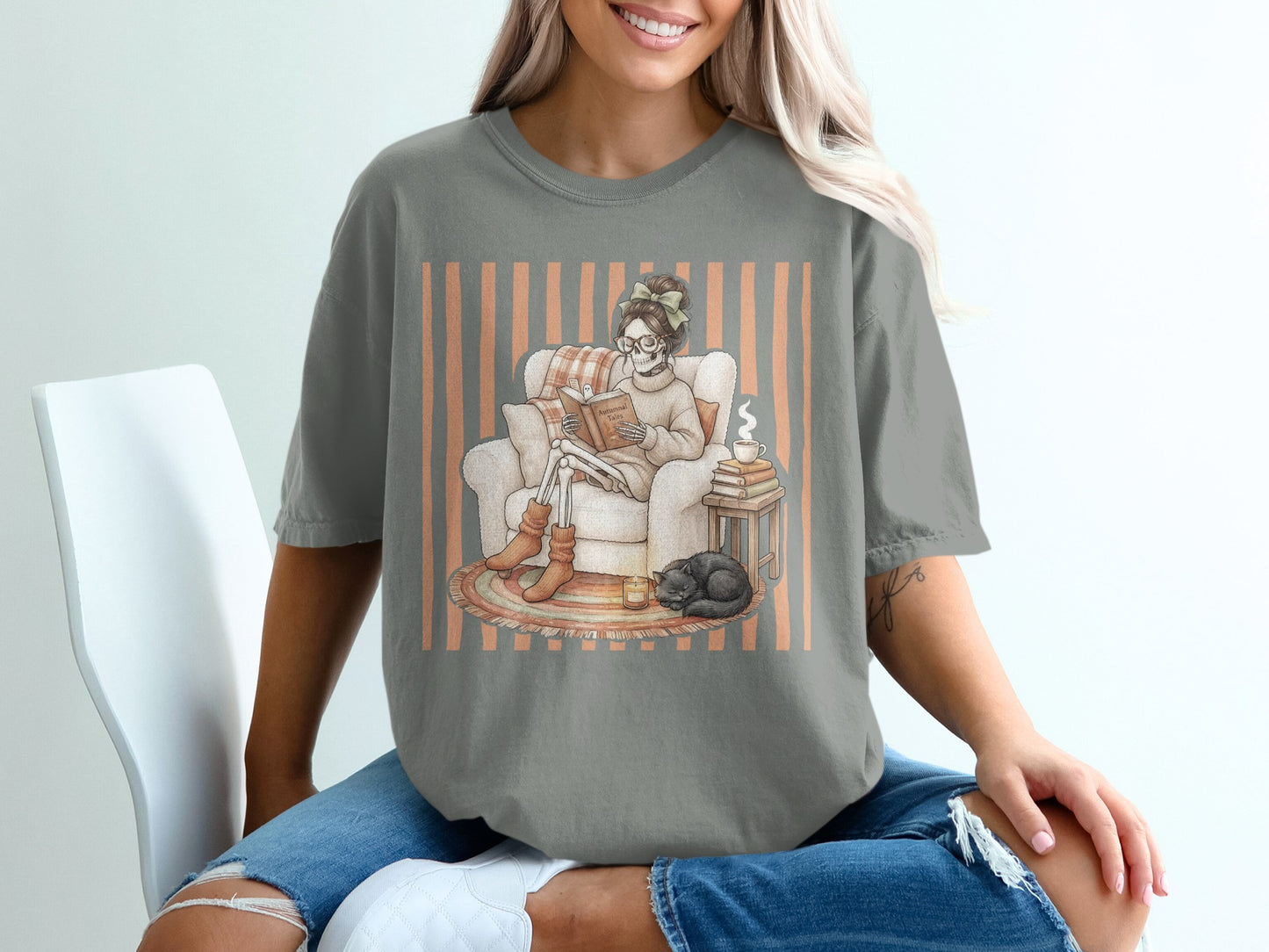 Skeleton reading "Autumnal Tales" with cat, candle, and coffee, on a t-shirt.