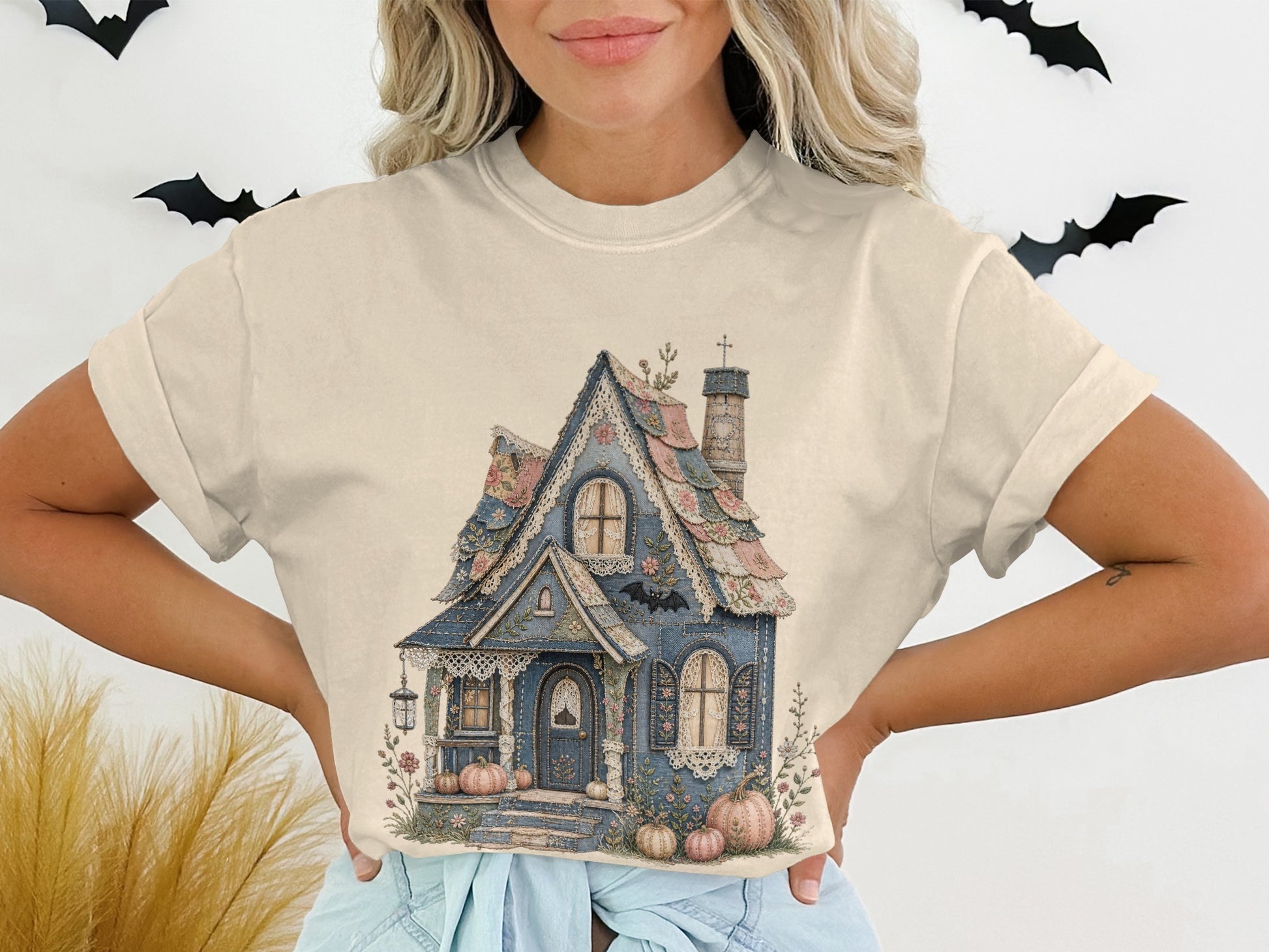 Cream t-shirt featuring an illustration of a blue cottage with pumpkins and bats.