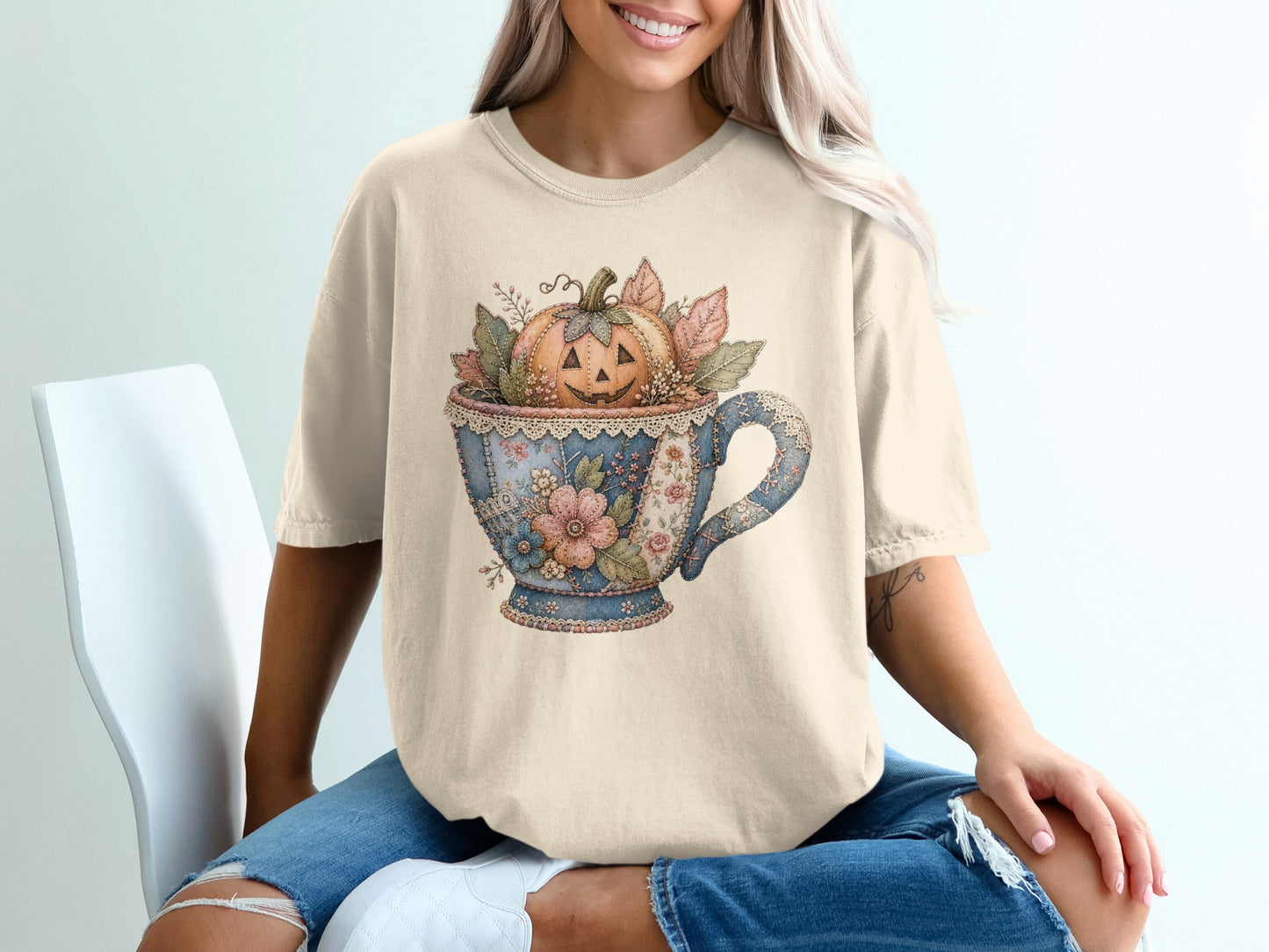 Cream t-shirt with a vintage teacup graphic filled with a jack-o'-lantern and autumn leaves.